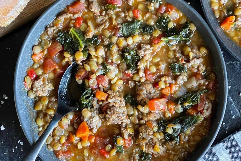 Lentil soup with sausage and spinach in a dark bowl.
