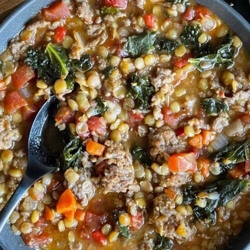 Lentil soup with sausage and spinach in a dark bowl.