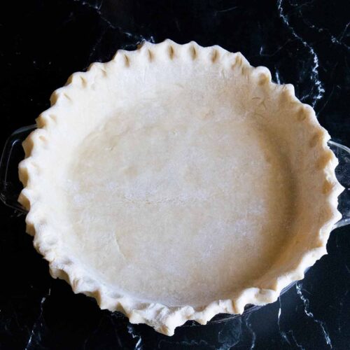 Fluted pie dough on a dark surface.