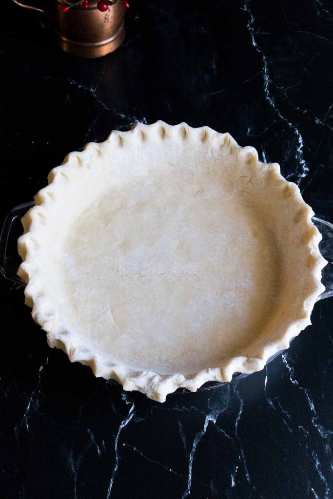 Fluted pie dough on a dark surface.