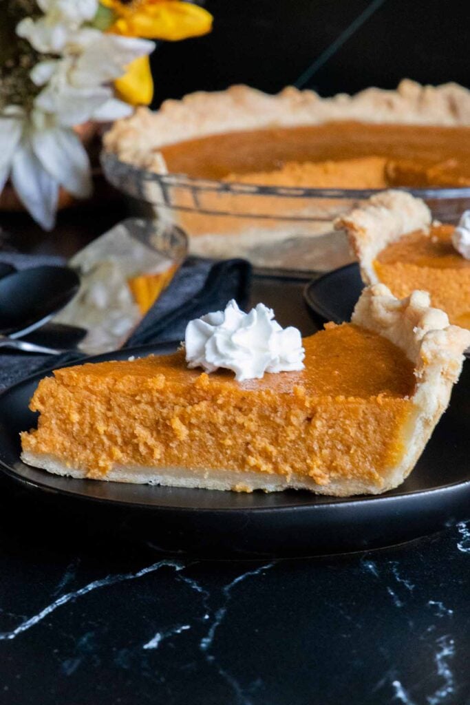 Southern sweet potato pie slices topped with whipped cream on black plates.