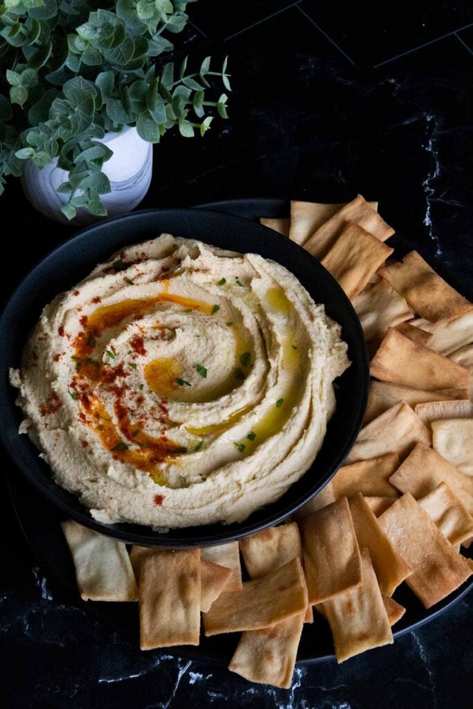 hummus in a black bowl surrounded by pita chips