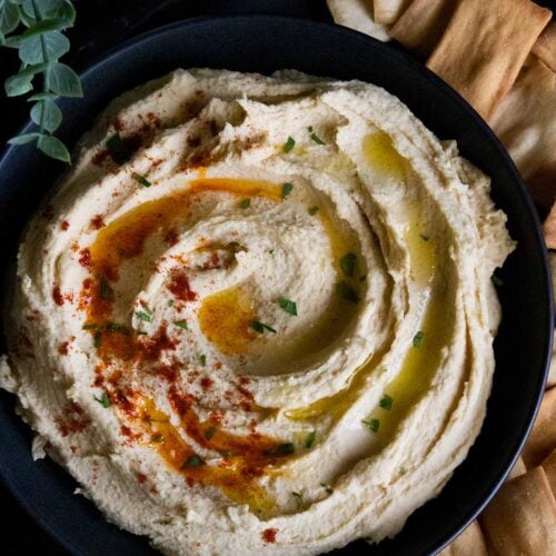 hummus in a black bowl surrounded by pita chips