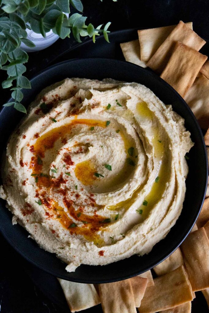 hummus in a black bowl surrounded by pita chips