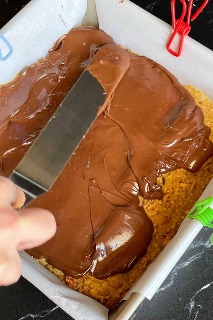 Melted chocolate being spread over the top of the peanut butter pretzel bars.