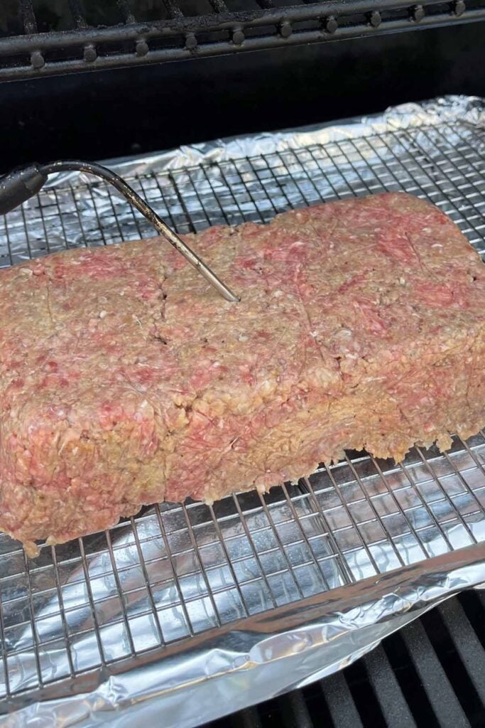 uncooked meatloaf on the smoker with a temperature probe inserted.