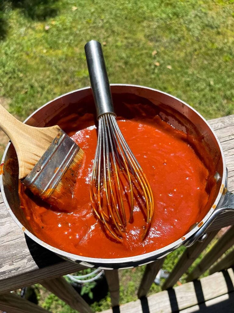 bourbon chipotle barbecue sauce in a saucepan with a whisk and brush.