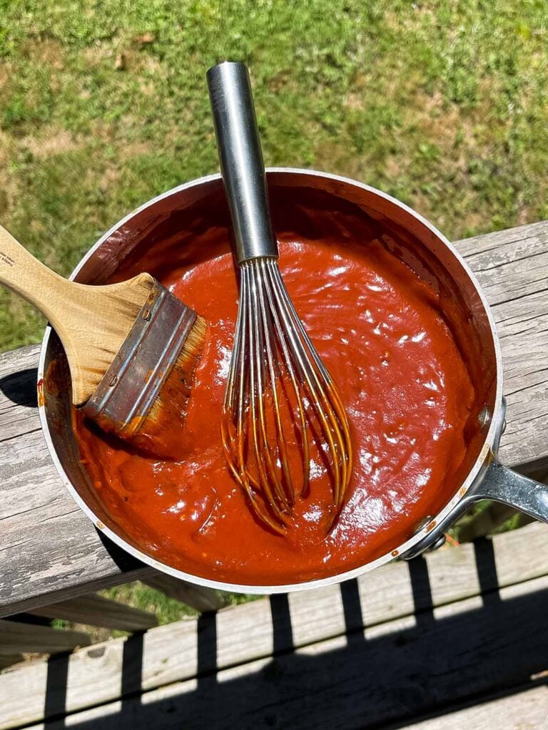 homemade bbq sauce in a saucepan resting on a deck rail.