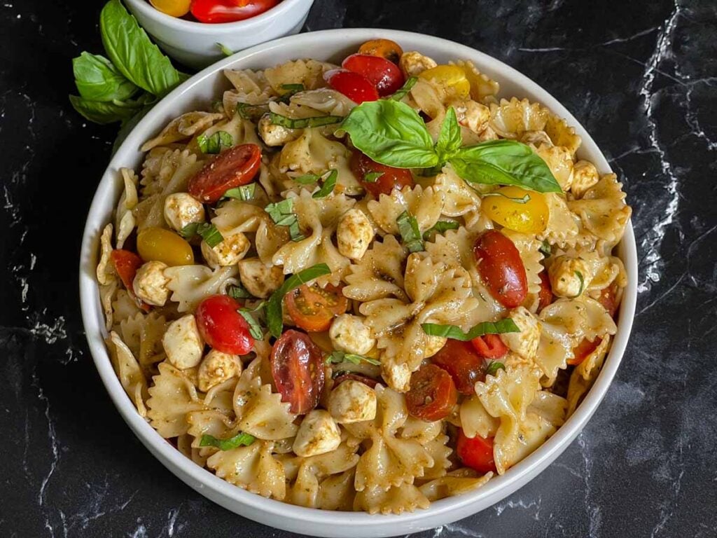 Pesto pasta Caprese salad in a white bowl.