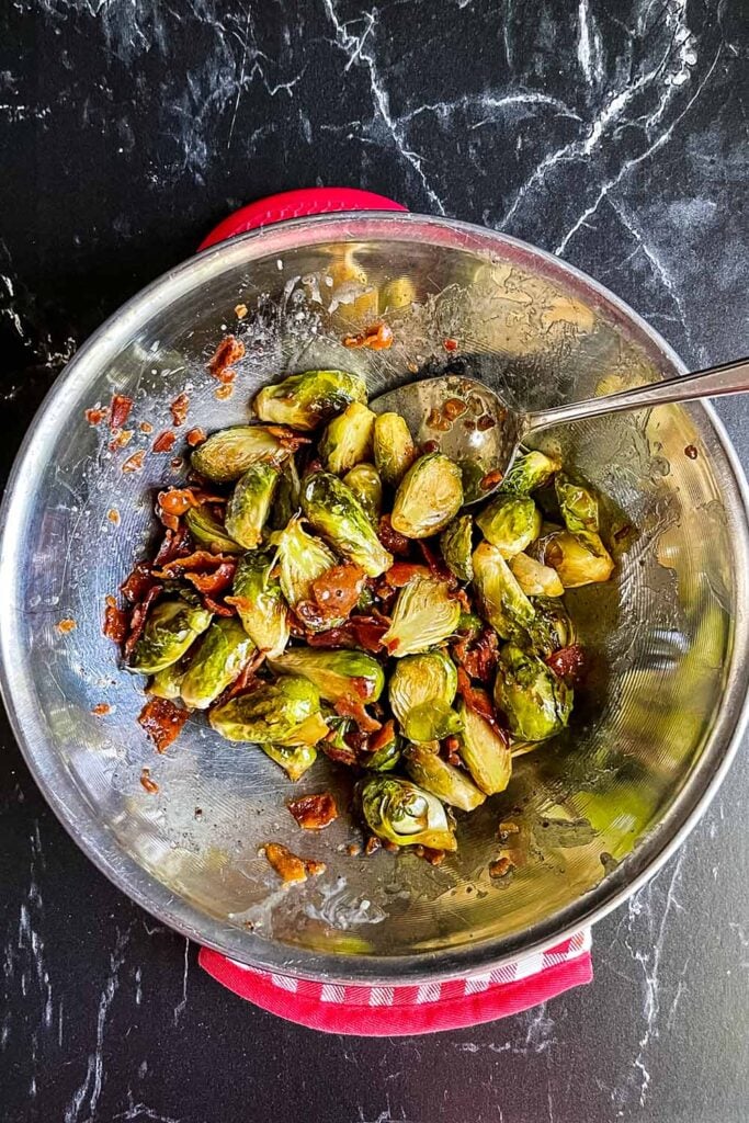 Roasted brussels sprouts with honey butter and bacon in a stainless steel bowl.