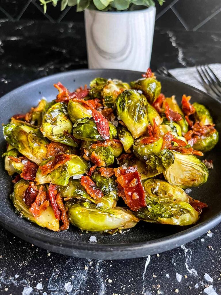 A plate of roasted brussels sprouts with honey butter and bacon.