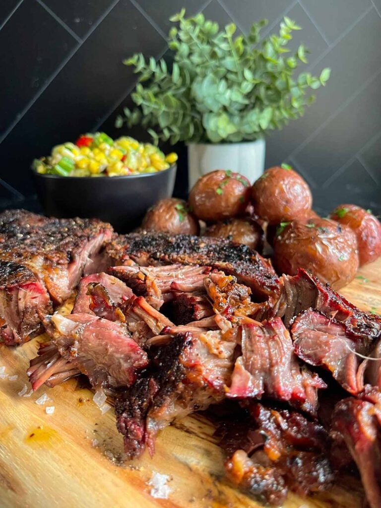 smoked chuck roast with summer succotash and grilled potatoes on a wooden board.