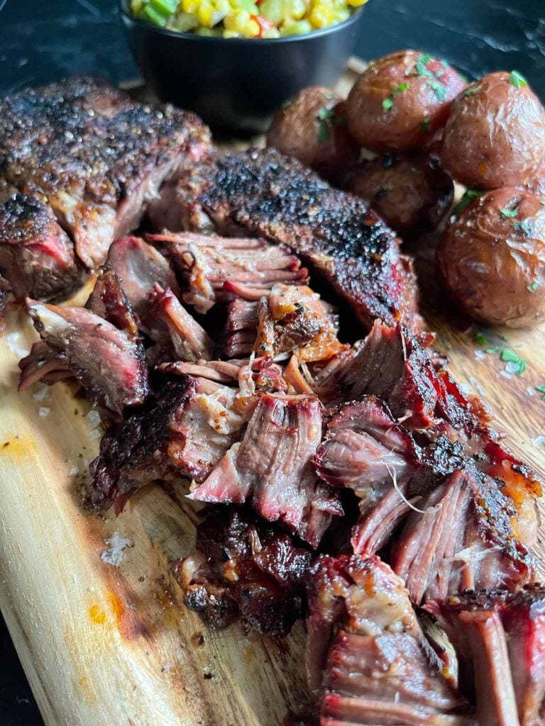 Smoked chuck roast with some grilled potatoes and succotash on a wooden board.