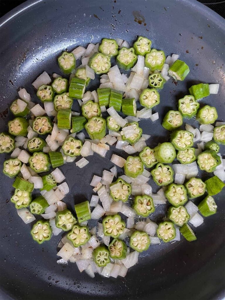 Diced onions and okra sautéing in a large skillet for summer succotash recipe.