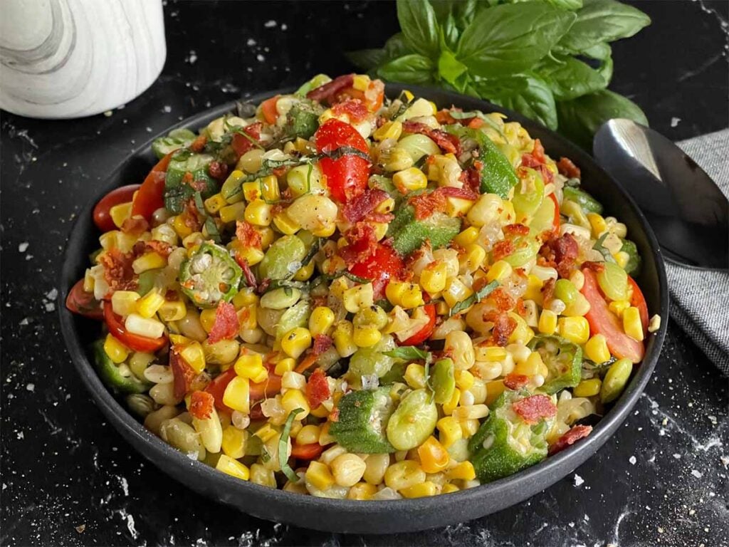 Summer succotash in a black bowl on a dark surface.