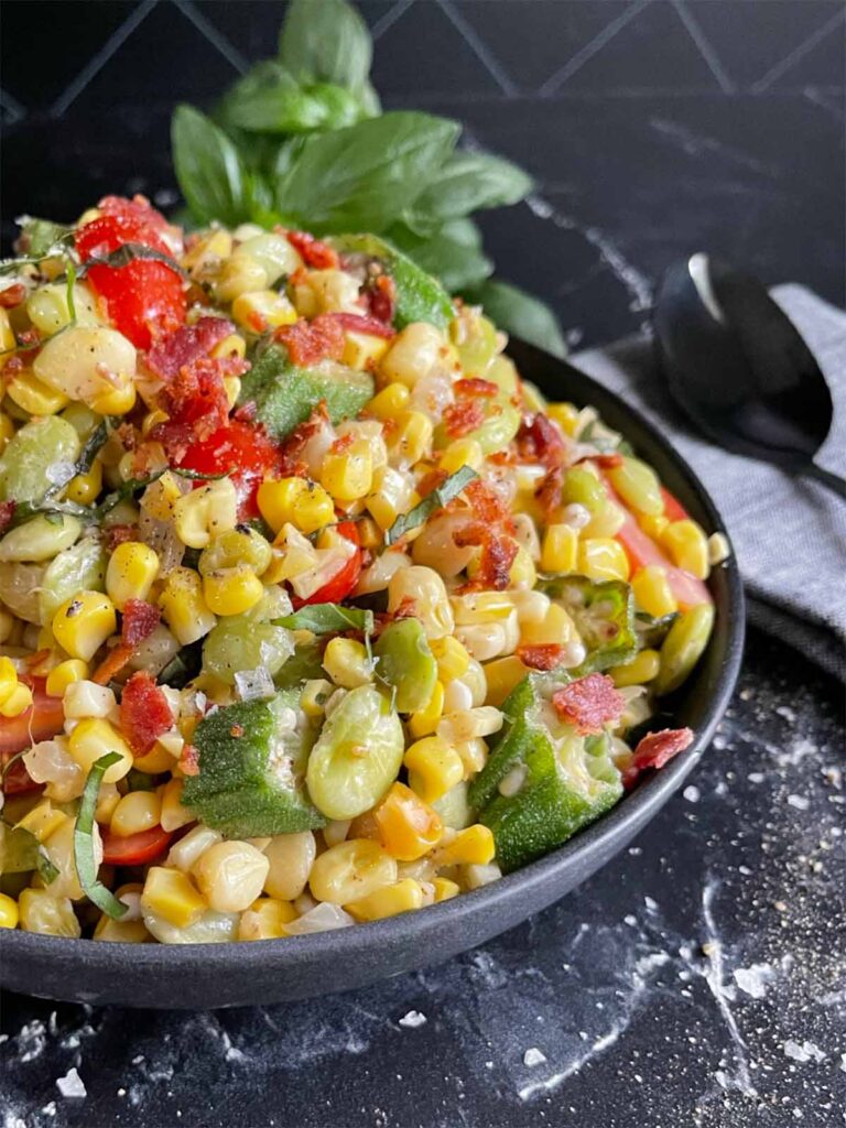 Succotash in a black bowl with a bunch of fresh basil in the background.