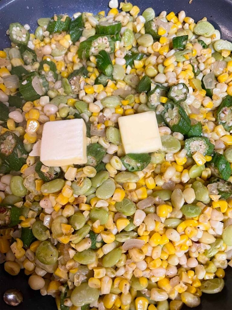 Succotash being cooked with unmelted pats of butter.