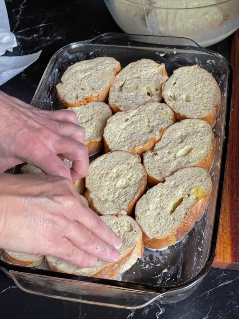 Placing dipped french toast into a baking dish.