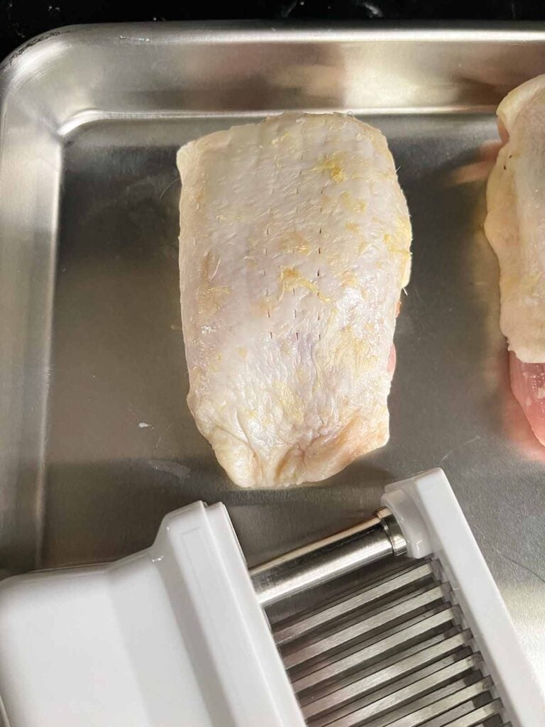 raw chicken thigh showing pierced skin from a meat tenderizer.