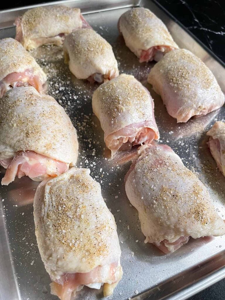 A tray of raw chicken thighs seasoned.