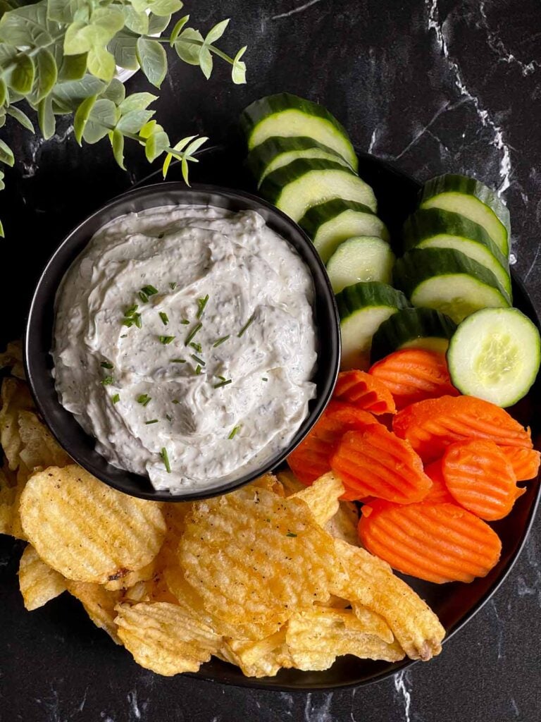 chip dip in a black bowl surrounded by chips and vegetables