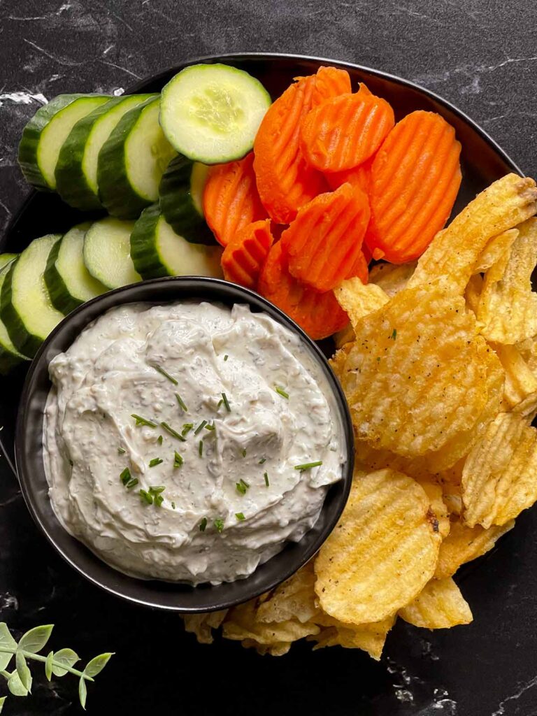 chip dip in a black bowl surrounded by chips and vegetables