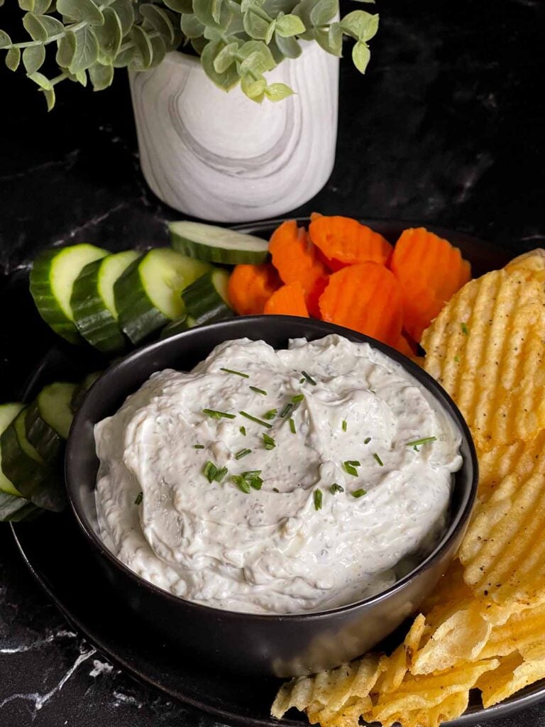 chip dip in a black bowl surrounded by chips and vegetables