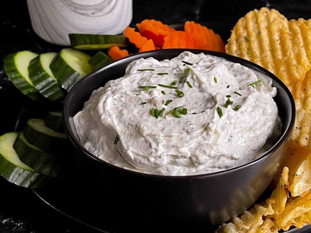 Chip dip in a black bowl surrounded by chips and vegetables