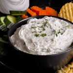 Chip dip in a black bowl surrounded by chips and vegetables