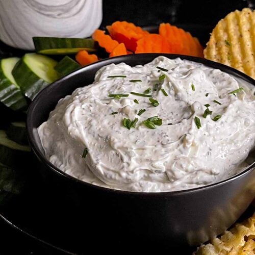 Chip dip in a black bowl surrounded by chips and vegetables