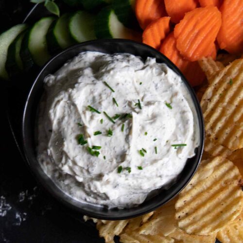 chip dip in a black bowl surrounded by chips and vegetables