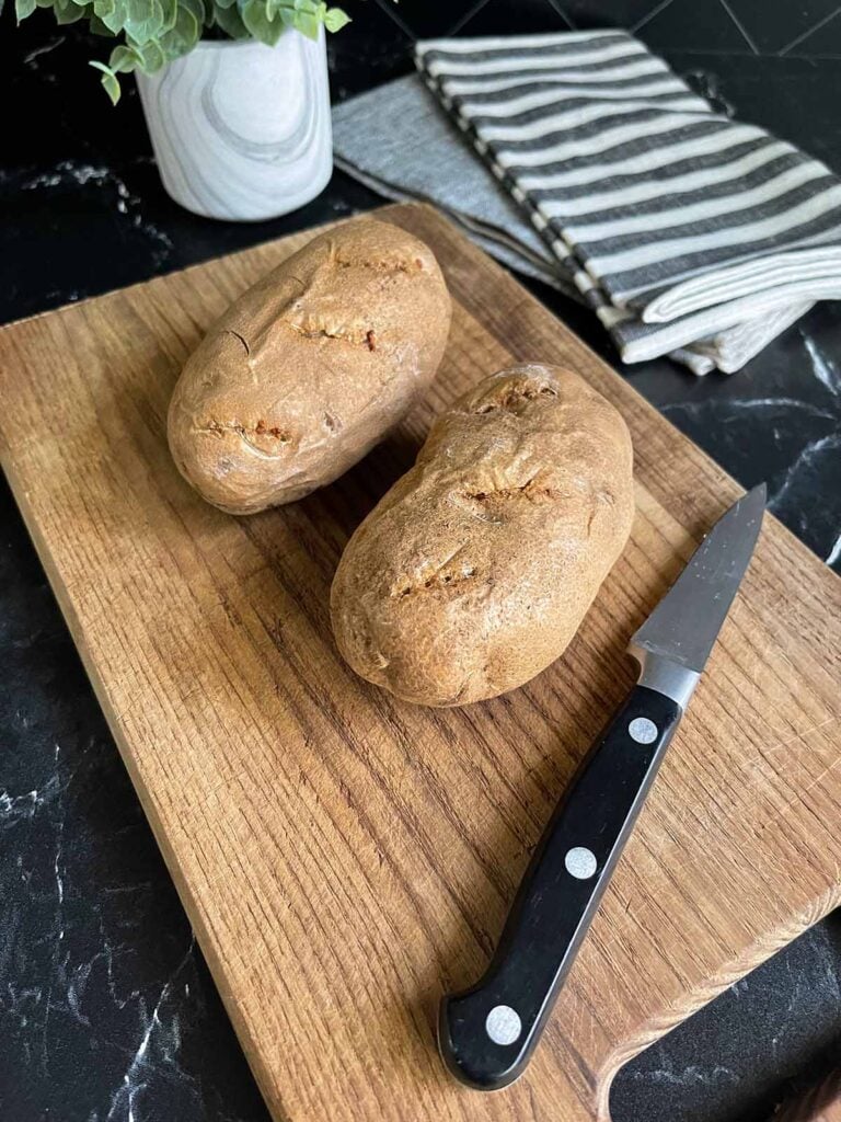 two baked potatoes on a cutting board