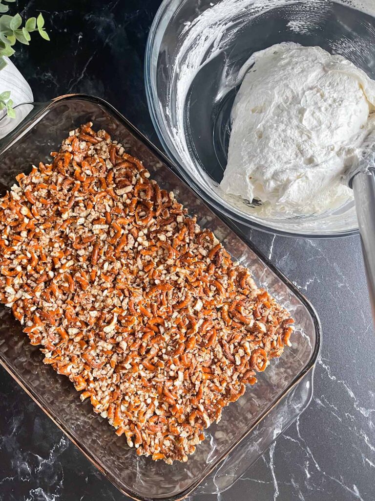 Pretzel crust in a 9x13 baking dish with a bowl of a whipped cream filling next to it.