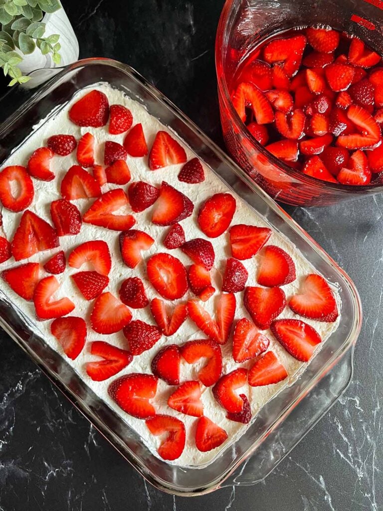 Fresh strawberry slices laying on top of a whipped cream and cream cheese topping.