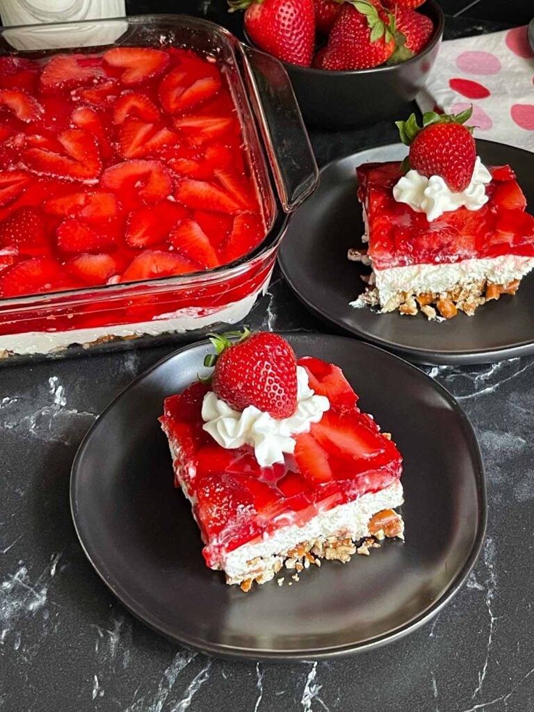 A couple slices of strawberry pretzel salad on black plates.