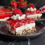 Slice of strawberry pretzel salad on black plates garnished with whipped cream and a fresh strawberry.