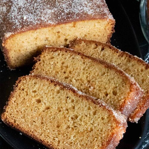 Apple cider doughnut loaf cake sliced on a black platter.