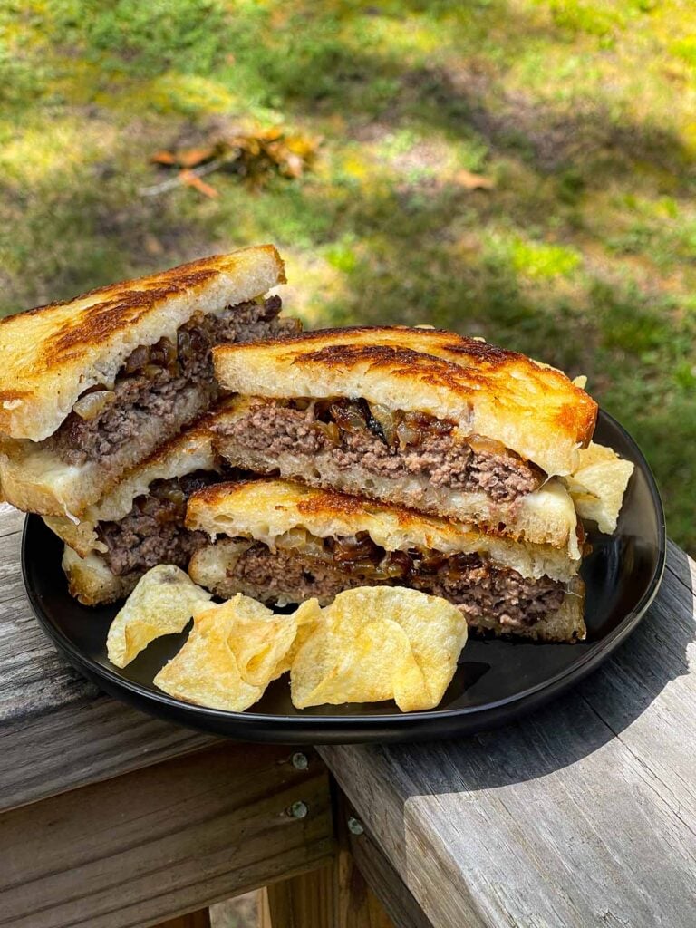 A patty melt on a black plate with chips as a side.