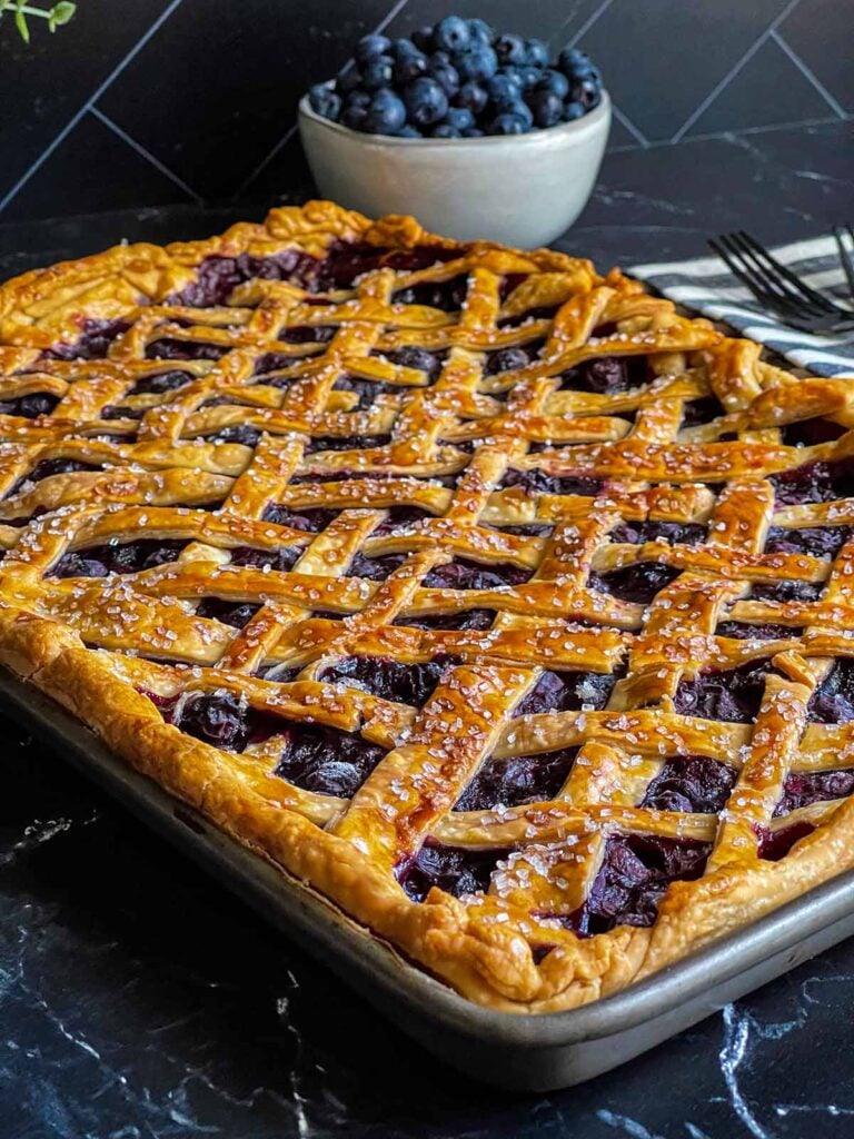 Blueberry slab pie in baking pan with a bowl of blueberries behind it.