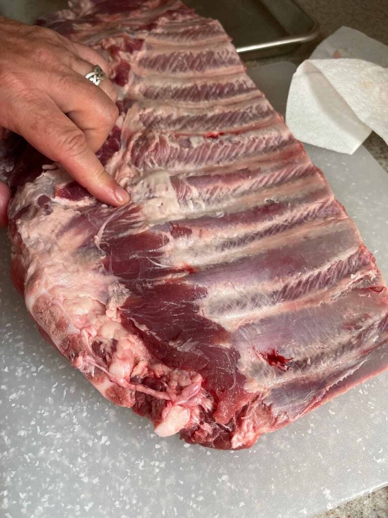 Identifying the proper location to cut to remove the brisket bone from the rack of ribs.