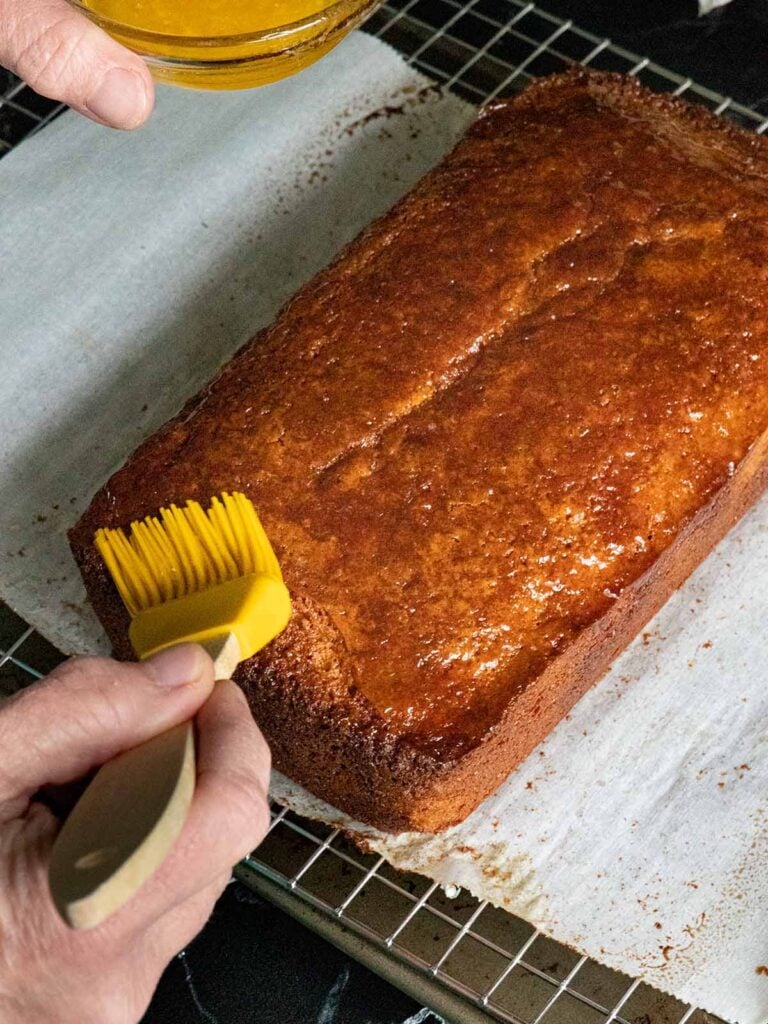 Brushing melted butter across the apple cider donut cake with a yellow brush.
