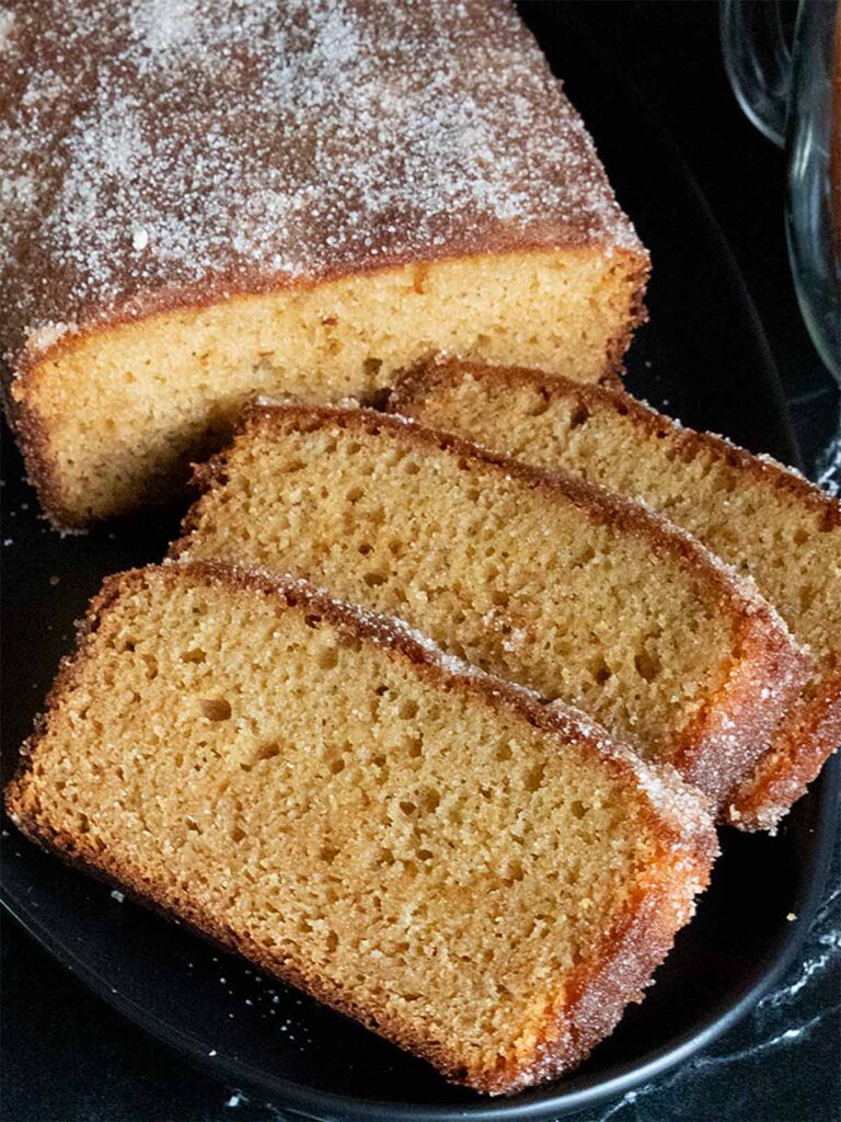 Apple cider doughnut loaf cake with three slices on a black plate.