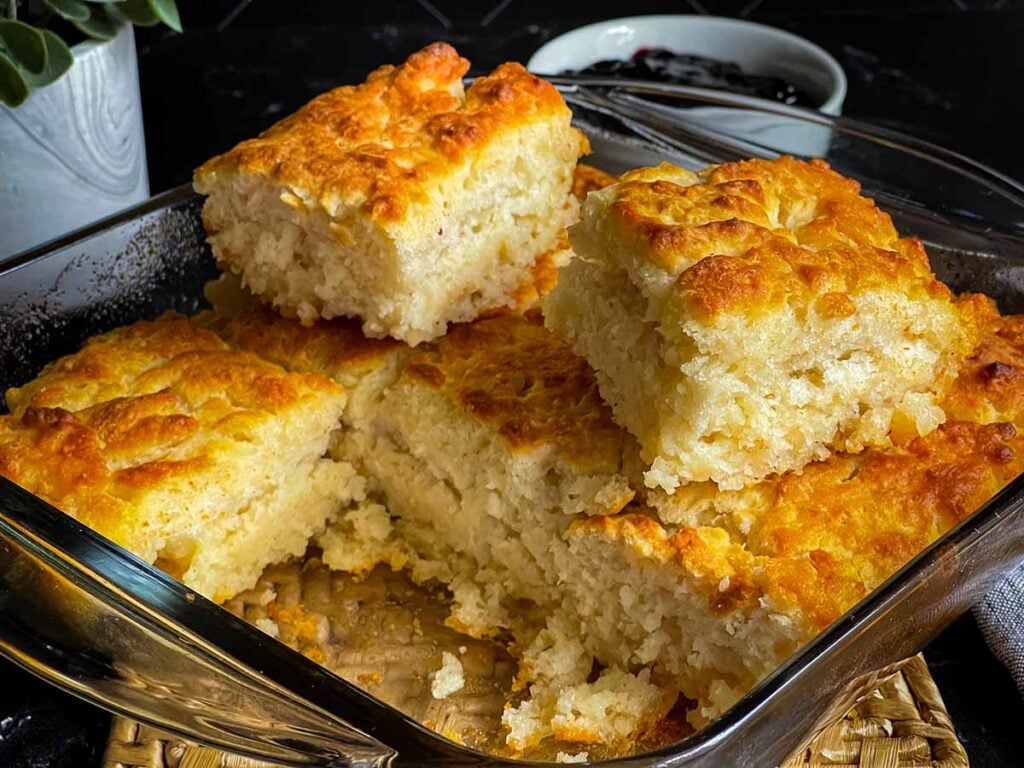 Two butter swim biscuits sitting on top of the pan of biscuits cut into squares.