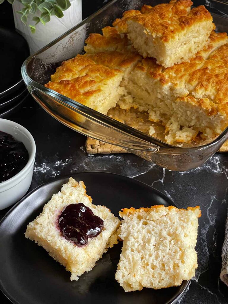 Butter swim biscuit cut in half with blackberry jam on one side on a black plate.