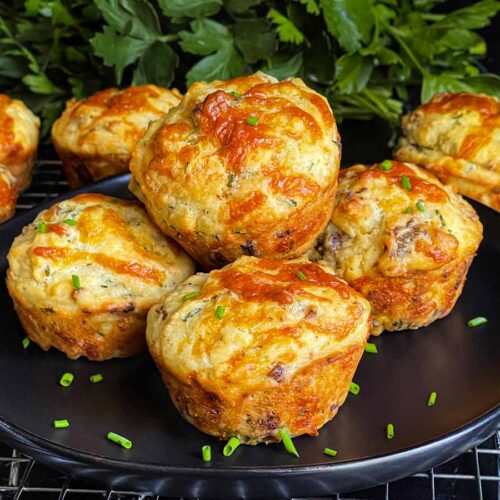 Sausage muffins stacked on a black plate garnished with diced chives.