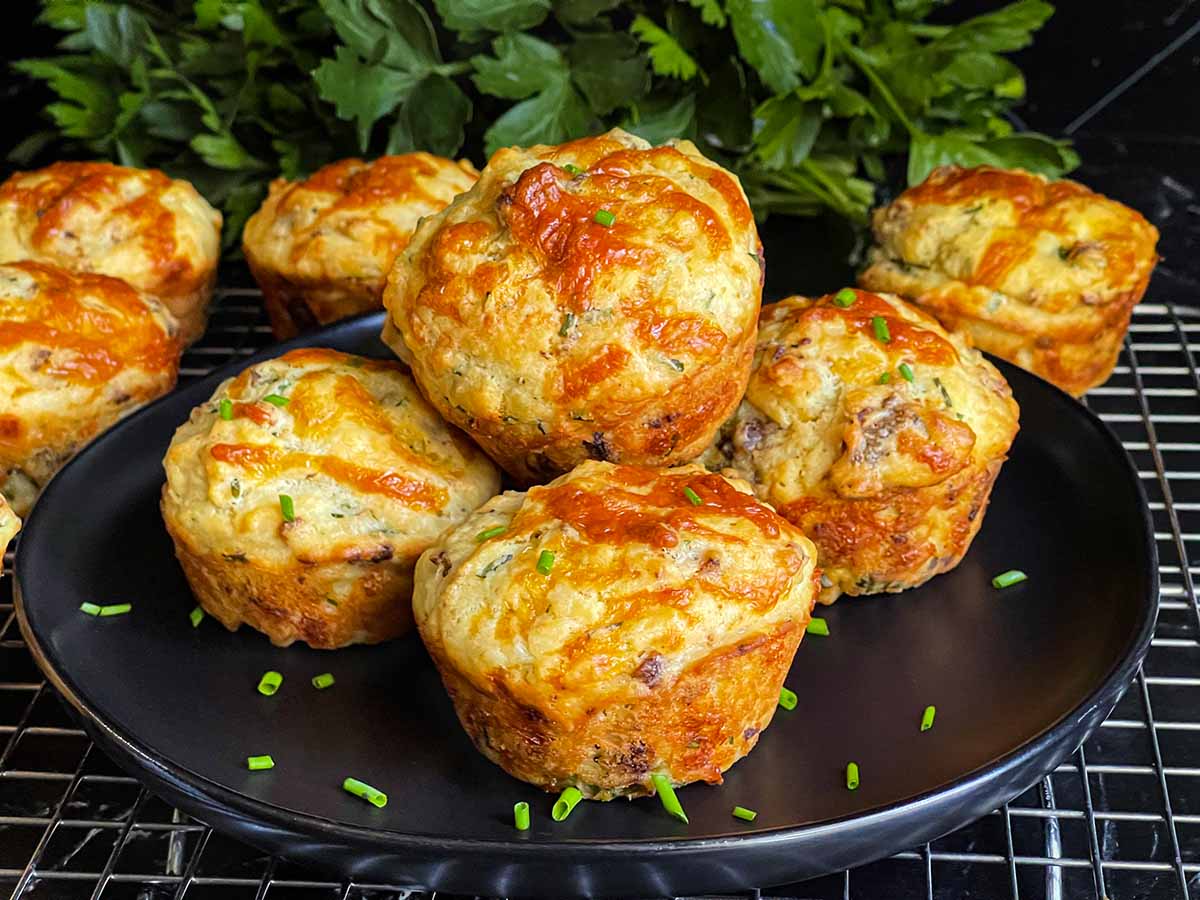 Sausage muffins stacked on a black plate garnished with diced chives.