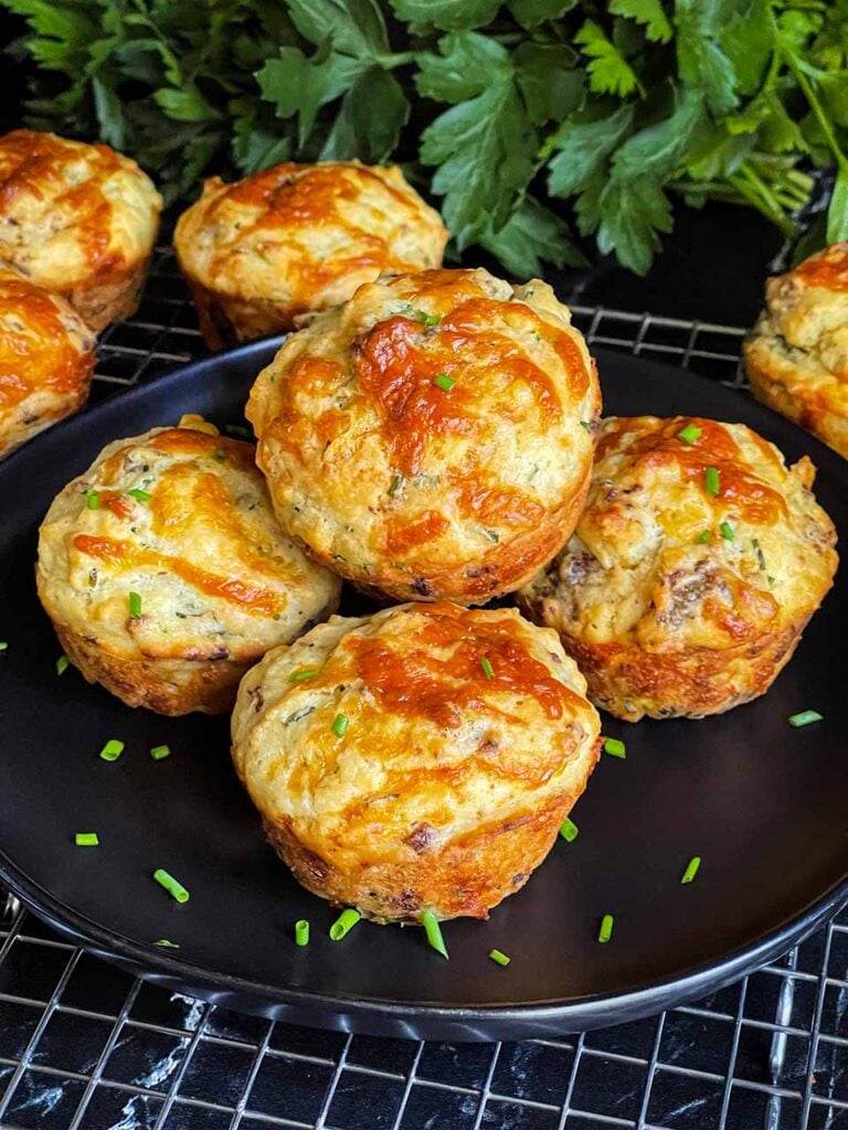 Sausage muffins stacked on a black plate garnished with diced chives.