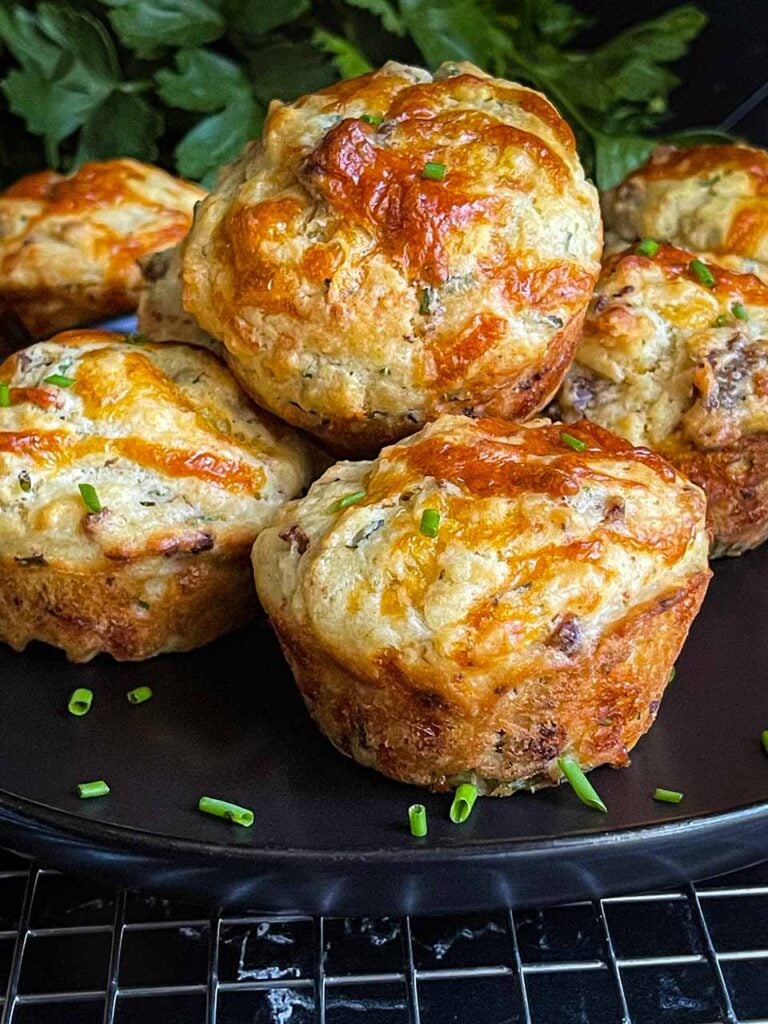 Sausage muffins stacked on a black plate garnished with diced chives.