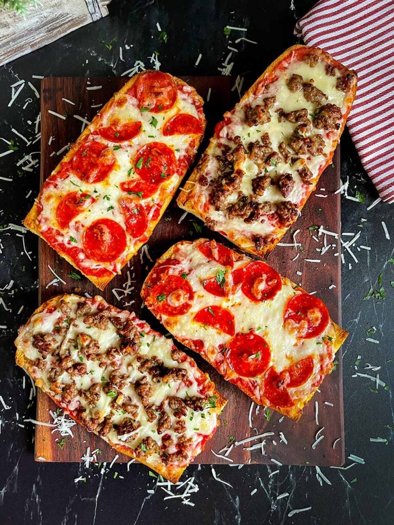 French bread pizza with italian sausage and pepperoni on a dark cutting board.