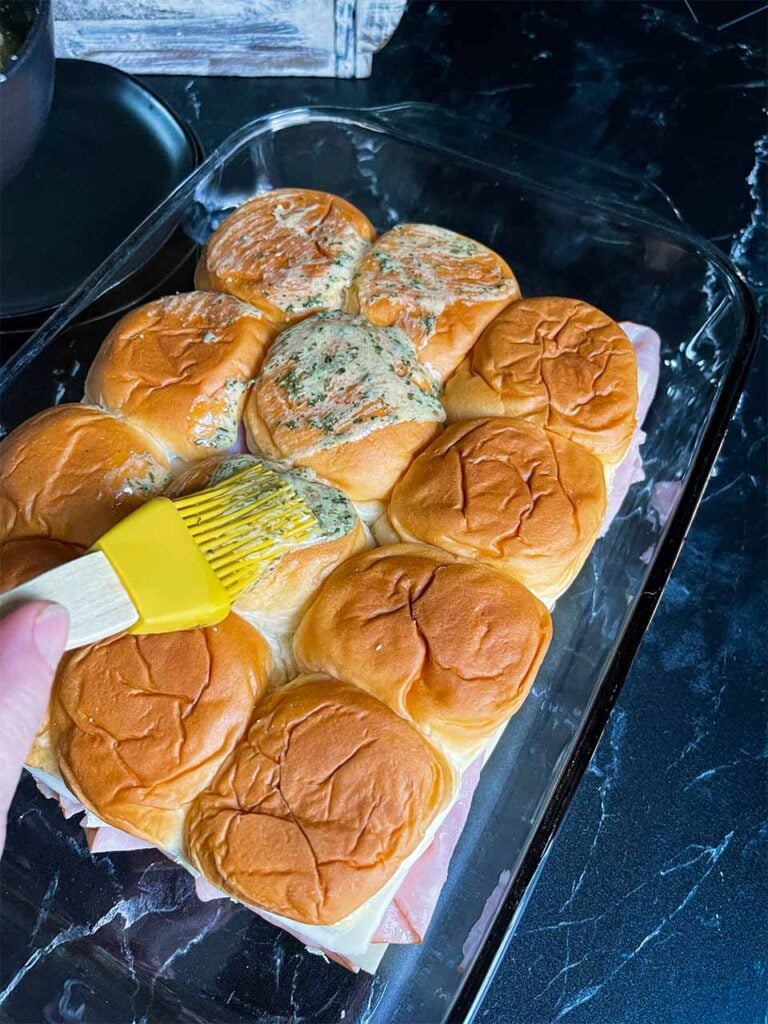 Brushing the butter mixture on top of the ham and swiss sliders.